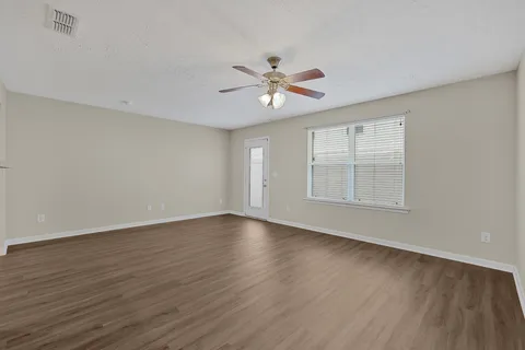 an empty room with wooden floor ceiling fan and windows