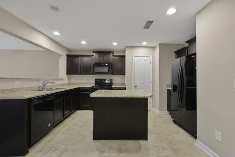 a large kitchen with stainless steel appliances kitchen island granite countertop a refrigerator and a sink