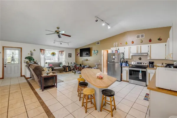 a kitchen with stainless steel appliances kitchen island granite countertop a refrigerator a stove a sink with white cabinets and wooden floor