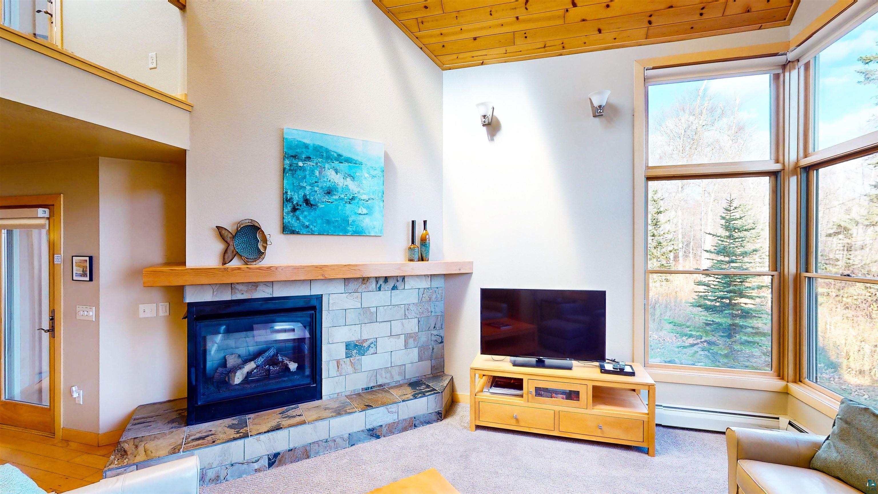 40 Surfside Drive, Unit 5D Tofte, MN 55615 - Photo 28 of 37 Living area featuring a stone and tile fireplace with a wood mantle, large windows, wood-finish ceiling, and a secondary upper-level opening