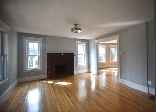 an empty room with wooden floor fireplace and windows