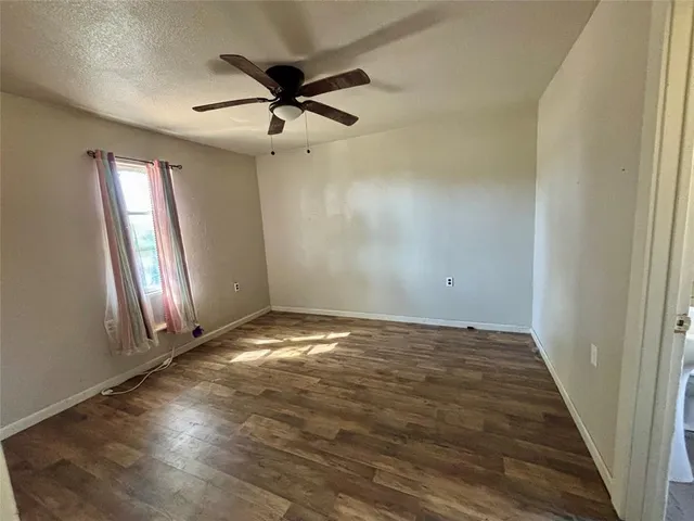 an empty room with wooden floor fan and windows