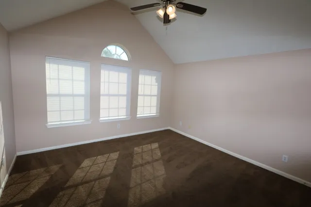 an empty room with chandelier fan and windows