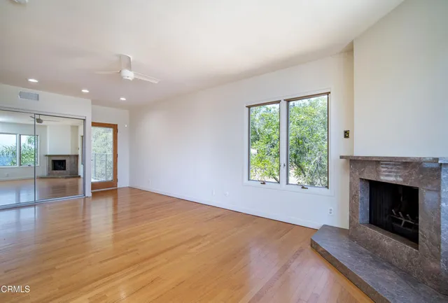 an empty room with wooden floor fireplace and windows