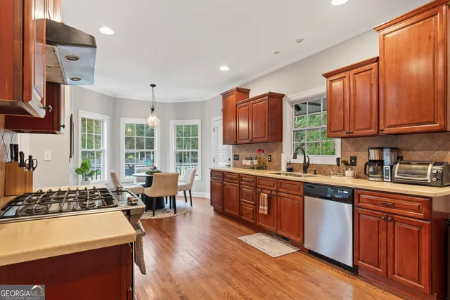 a kitchen with stainless steel appliances granite countertop wooden cabinets a sink dishwasher a stove and a refrigerator with wooden floor