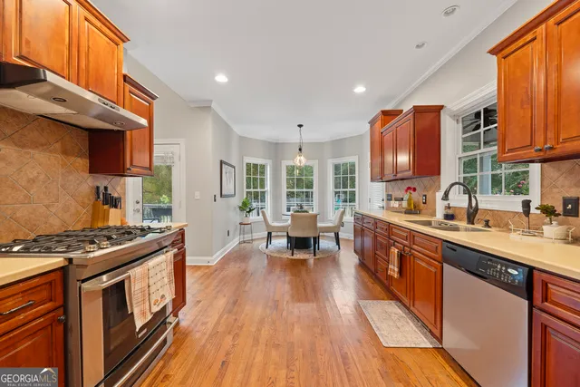 a kitchen with stainless steel appliances a stove a sink dishwasher a refrigerator white cabinets and wooden floor