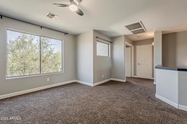 an empty room with a chandelier fan and windows