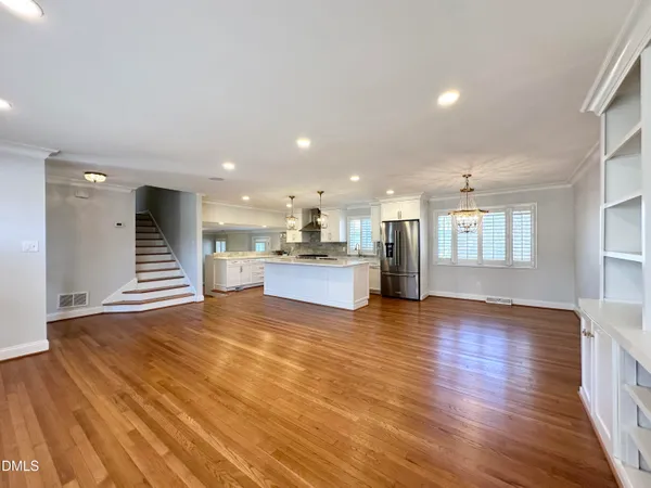 a view of an empty room with wooden floor and kitchen