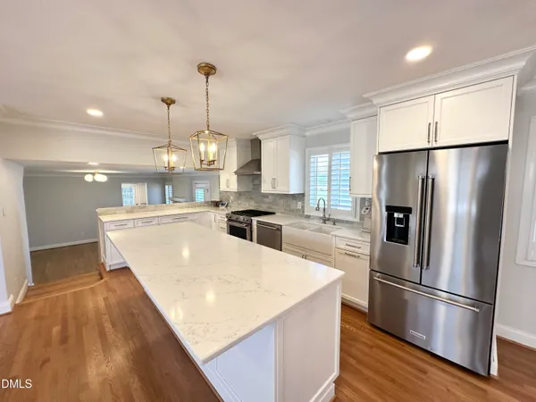 a kitchen with stainless steel appliances granite countertop a refrigerator a sink dishwasher a oven and a dining table with wooden floor