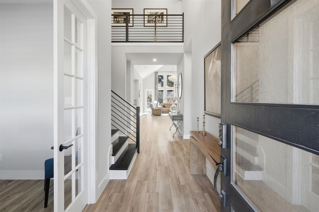 8408 Twistpine Road Frisco, TX 75035 - Photo 5 of 38 Two-story entryway featuring a black frame front door with textured glass, wood-finish flooring, a contemporary staircase with horizontal metal railings, and a second-level open hallway with matching railings