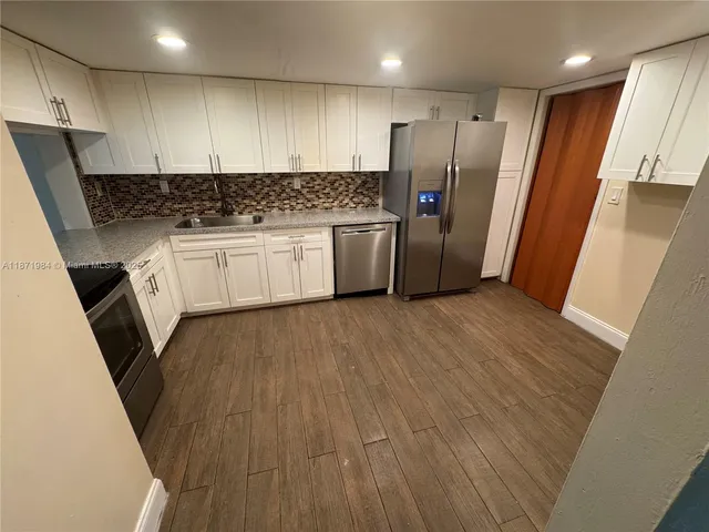 a kitchen with granite countertop a refrigerator a sink and wooden floors