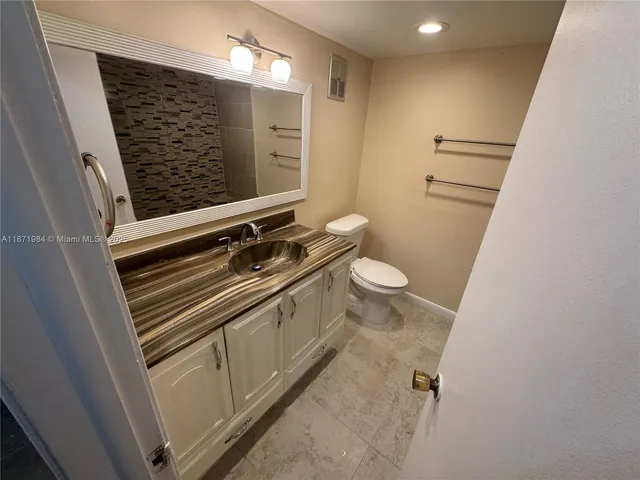 a bathroom with a granite countertop sink a toilet a mirror and shower