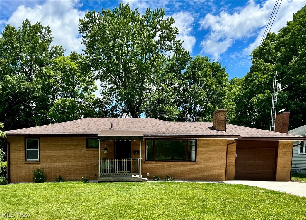 Brick ranch-style residence featuring an attached garage with a brown panel door, a covered front porch with white railings, and a brown shingle roof