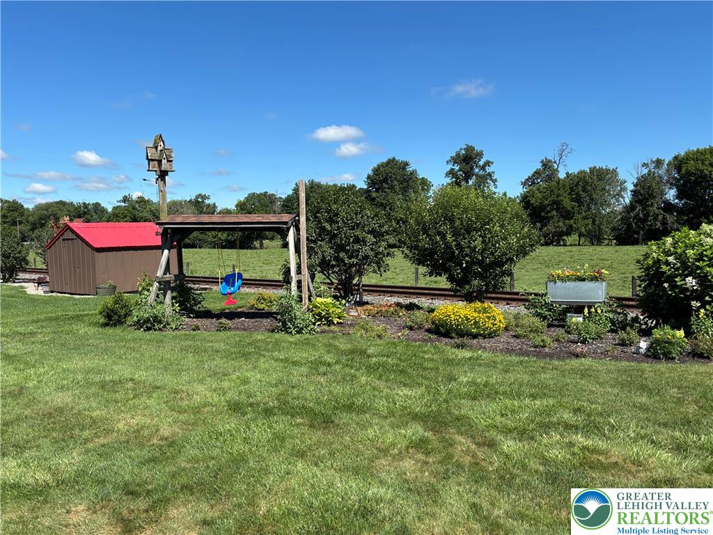 4938 Steuben Road Nazareth, PA 18064 - Photo 7 of 8 A tranquil yard features a storage shed and playset, set against a backdrop of green fields and a clear sky.