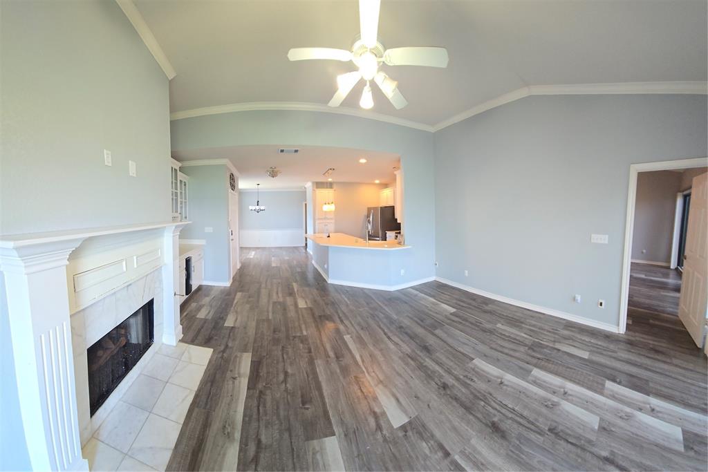 1904 Signal Ridge Place Rockwall, TX 75032 - Photo 2 of 23 Spacious living area featuring wood-finish flooring, a white mantel fireplace with a tile hearth, vaulted ceilings with crown molding, and an integrated ceiling fan