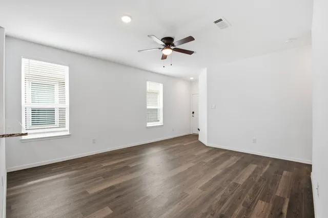 an empty room with wooden floor ceiling fan and windows