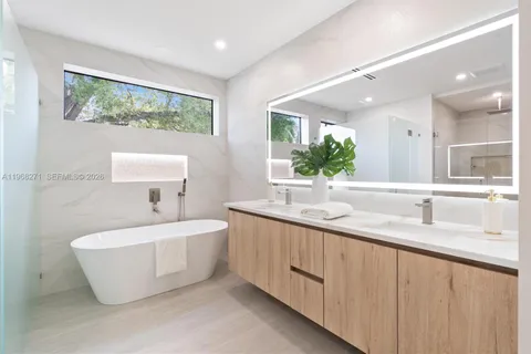 a bathroom with a double vanity sink a large mirror and a bathtub