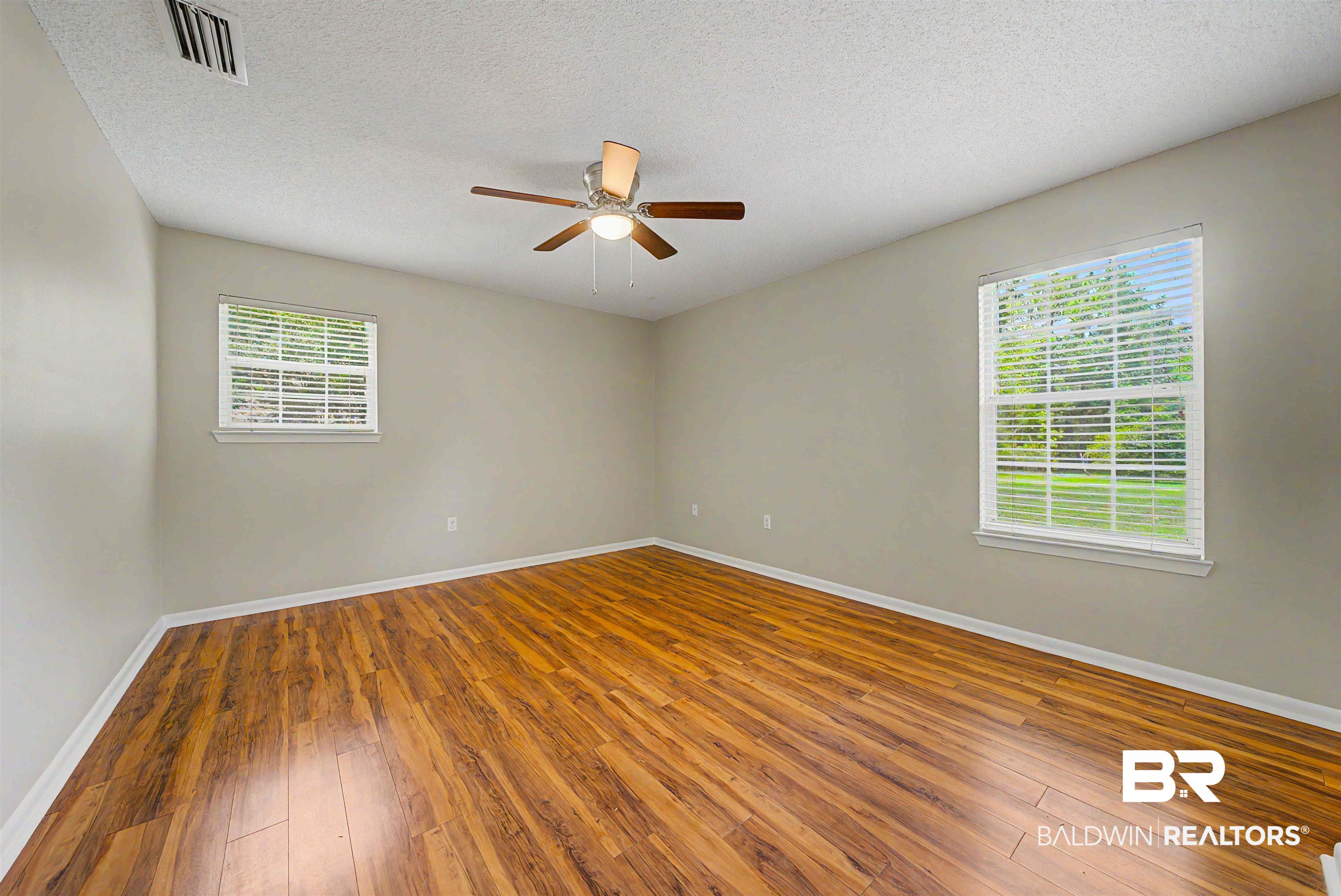 22963 Highway 98 Foley, AL 36535 - Photo 18 of 52 Spacious room featuring wood-finish flooring, two windows with blinds, a ceiling fan with integrated lighting, and neutral wall paint