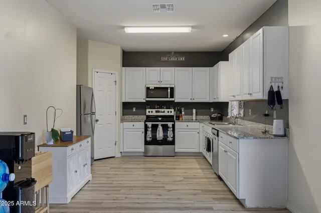 a kitchen with stainless steel appliances granite countertop a stove top oven a sink and white cabinets