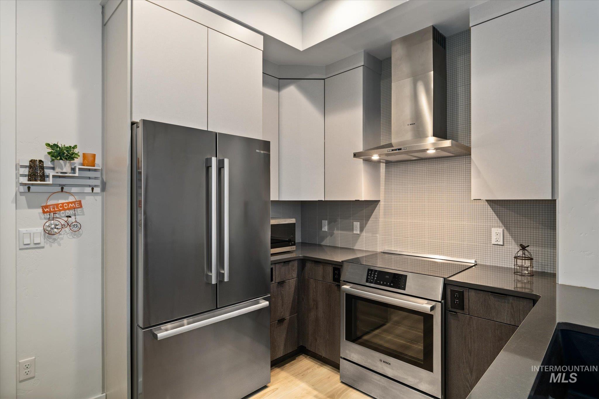 3850 East Haystack Street, Unit 302 Boise, ID 83716 - Photo 5 of 50 Kitchen with modern cabinets, appliances with stainless steel finishes, wall chimney range hood, backsplash, and light wood finished floors