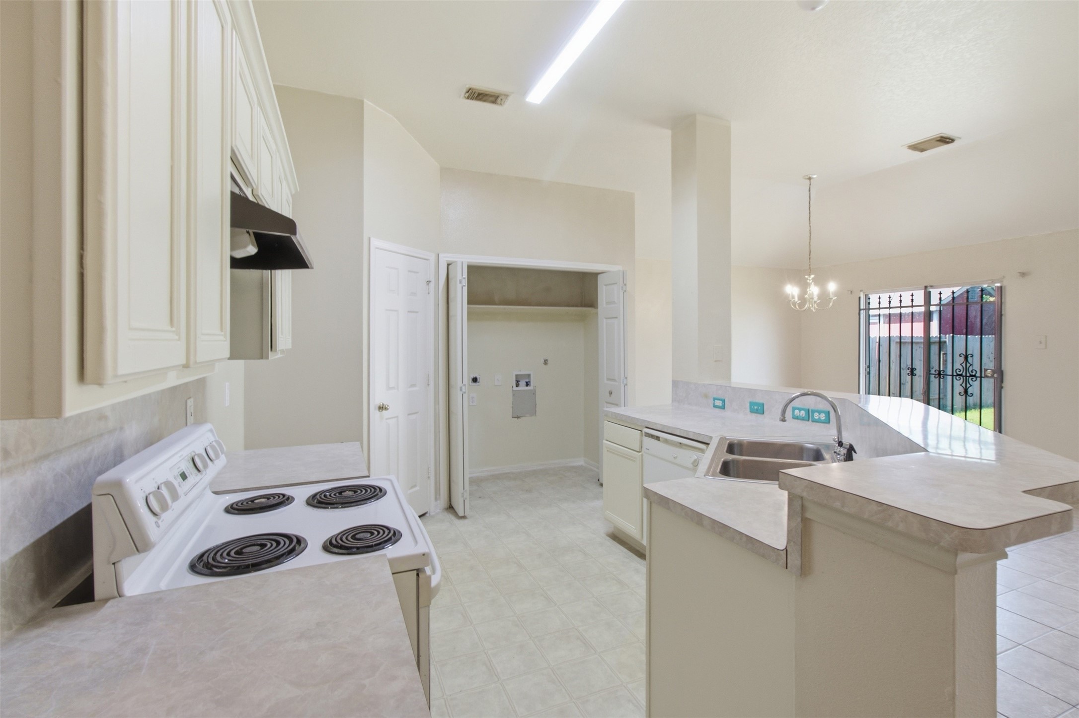 15738 Boonridge Road Houston, TX 77053 - Photo 16 of 31 Bright kitchen with ample counter space, electric stovetop, and breakfast bar, leading to a utility area and open dining space with chandelier and natural light.