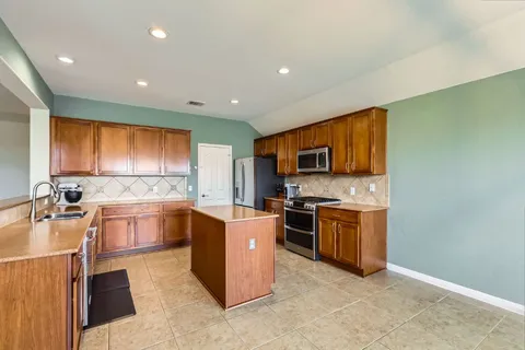 a large kitchen with stainless steel appliances granite countertop a stove top oven a sink dishwasher a refrigerator and cabinets with wooden floor