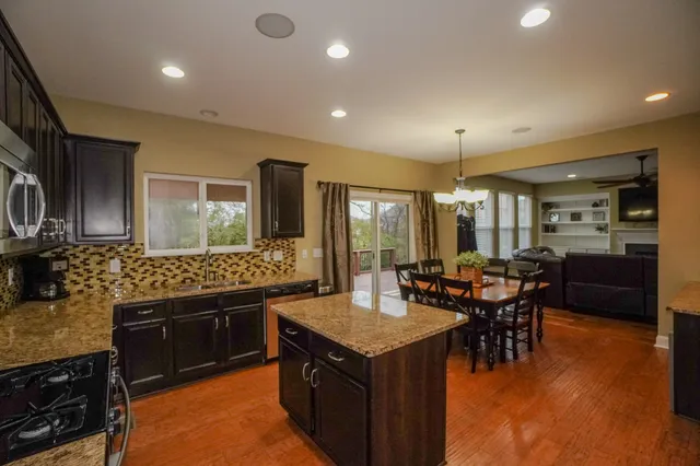 a kitchen with stainless steel appliances kitchen island granite countertop wooden cabinets stove top oven and sink