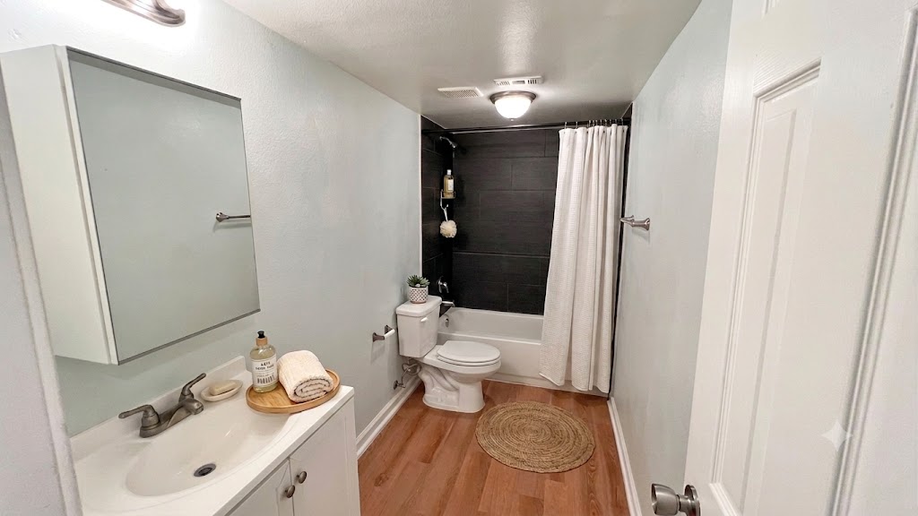 A compact, well-appointed bathroom featuring durable wood flooring and a classic tub-shower combination.