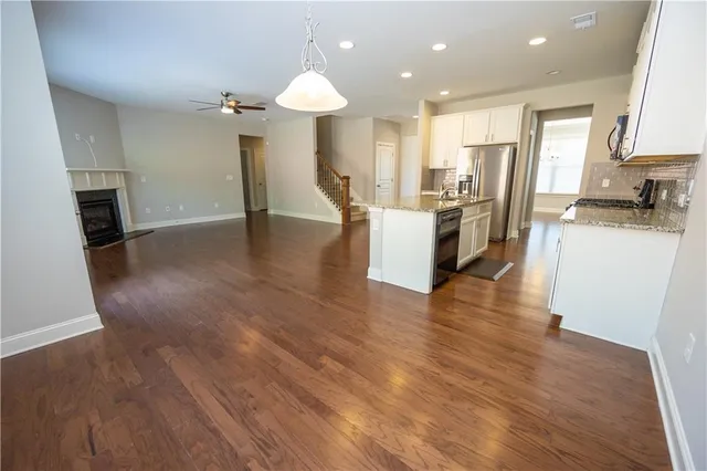 a open kitchen with kitchen island granite countertop a refrigerator oven a sink dishwasher and white cabinets with wooden floor