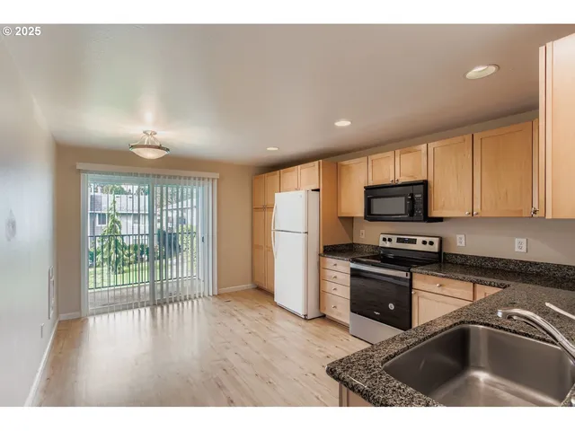 a kitchen with stainless steel appliances granite countertop a refrigerator a sink dishwasher a stove and white cabinets with wooden floor