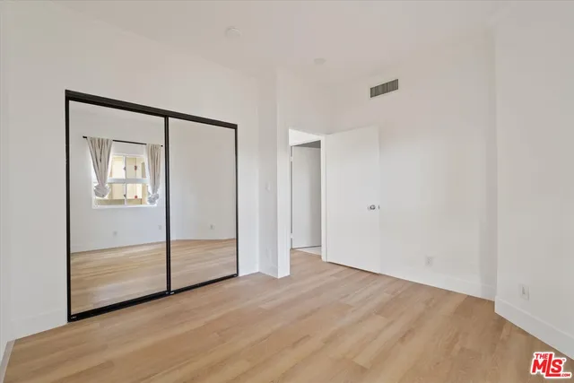 a view of an empty room with wooden floor and closet