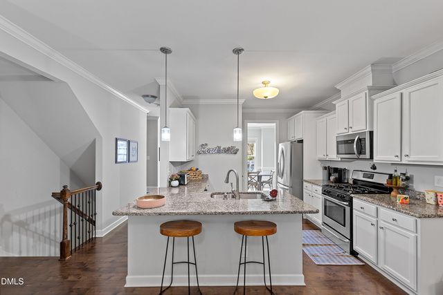 a kitchen with kitchen island granite countertop a stove a sink a dining table and chairs with wooden floor