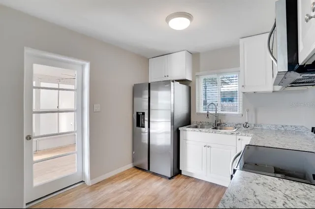 a kitchen with stainless steel appliances granite countertop a refrigerator a sink and white cabinets