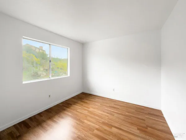 a view of an empty room with wooden floor and a window