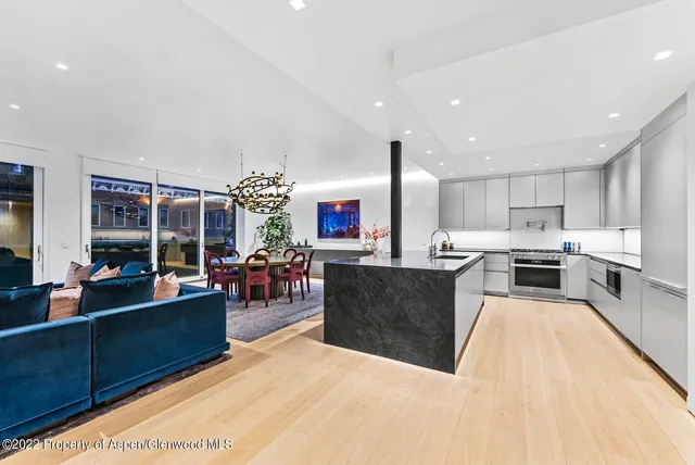 a kitchen with stainless steel appliances kitchen island granite countertop a refrigerator a stove top oven and a dining table with wooden floor