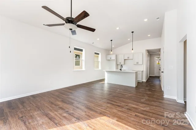 a view of an empty room and kitchen view with wooden floor