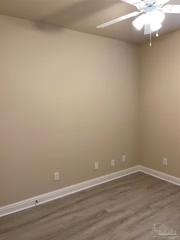 a view of an empty room with wooden floor and fan