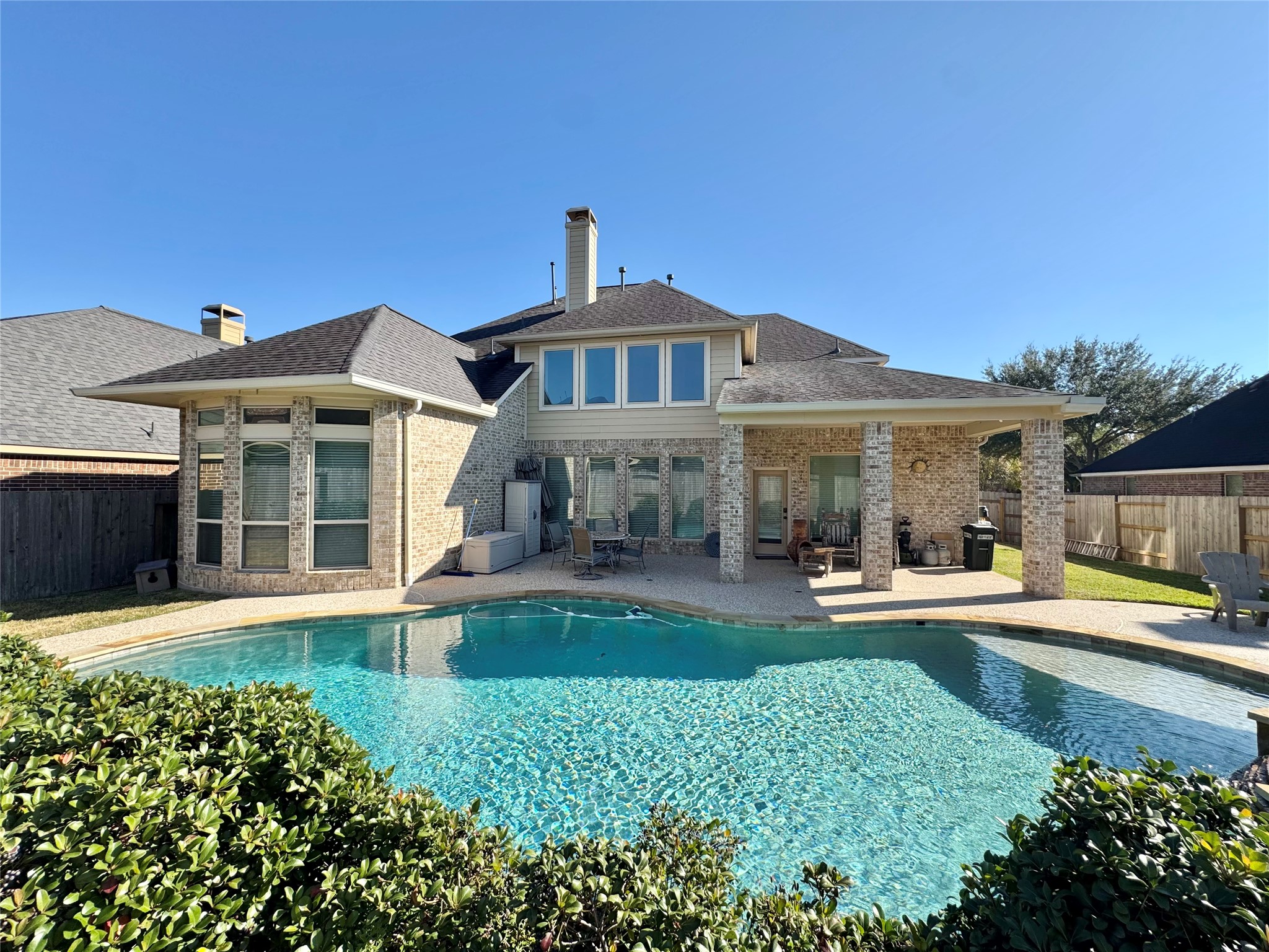 This spacious two-story home with a brick exterior and a beautiful backyard features a large swimming pool. The covered patio provides a perfect space for outdoor relaxation and entertaining.