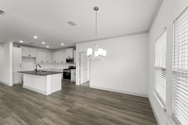 a large kitchen with kitchen island a sink dishwasher a refrigerator and white cabinets with wooden floor