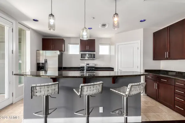 a kitchen with stainless steel appliances kitchen island granite countertop a stove a sink a refrigerator a dining table and chairs with wooden floor