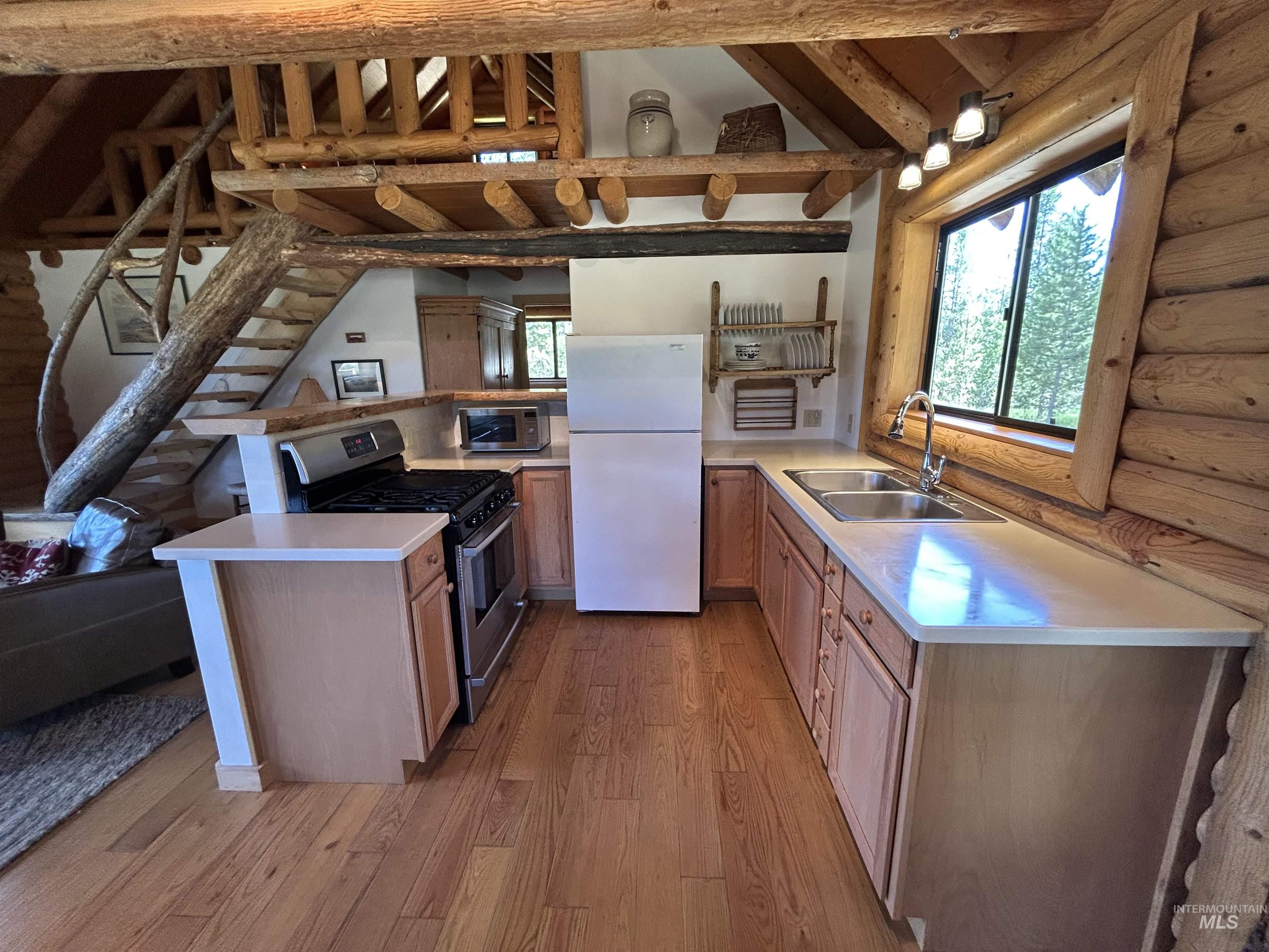 35 Sawtooth Way Stanley, ID 83278 - Photo 11 of 36 Rustic kitchen featuring log construction, wood-finish flooring, a stainless steel gas range, double basin sink, and ample counter space with upper and lower cabinetry