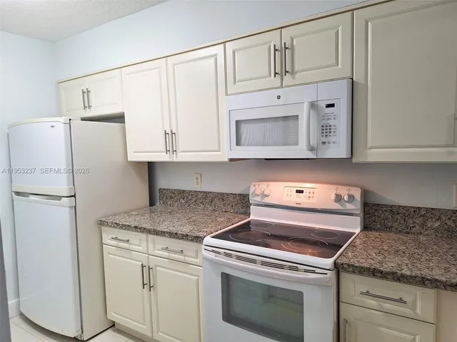 a kitchen with granite countertop white cabinets and white appliances