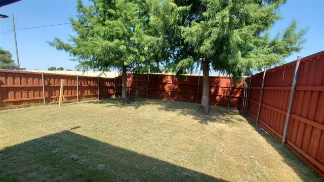 a view of a backyard with wooden fence and large trees