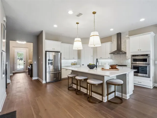 a kitchen with stainless steel appliances kitchen island granite countertop a table chairs and a wooden floor