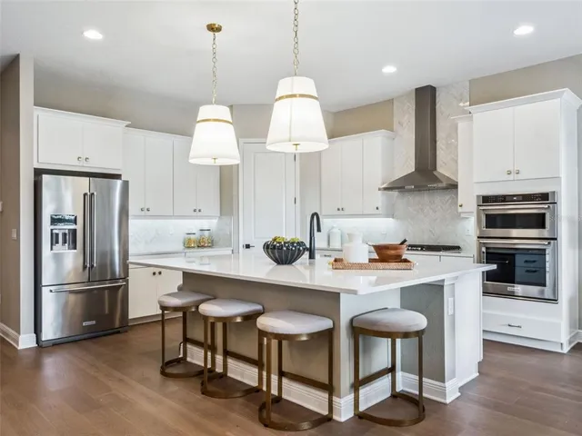 a kitchen with stainless steel appliances granite countertop a stove a refrigerator a sink dishwasher a dining table and chairs with wooden floor