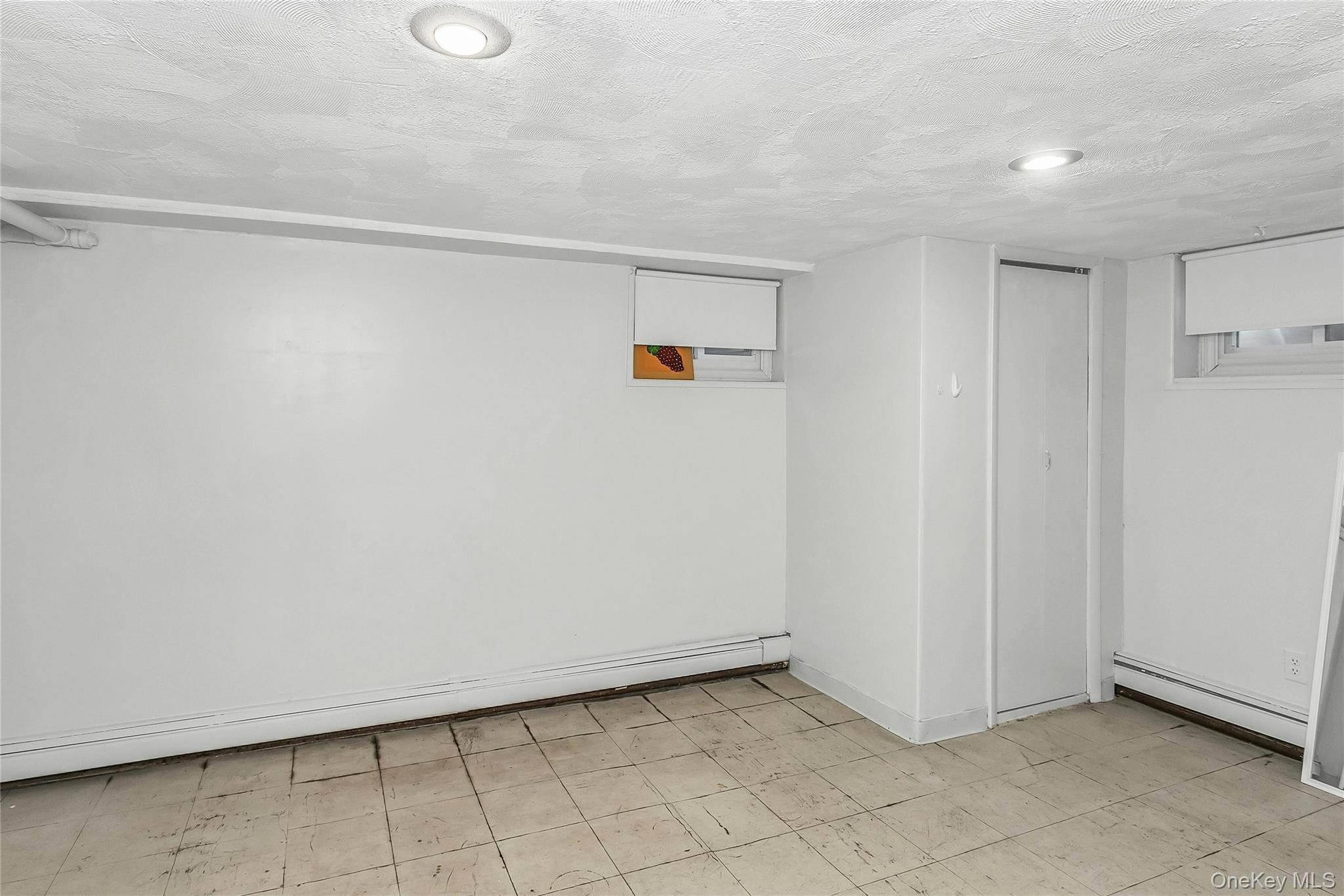622 Wellelein Road Uniondale, NY 11553 - Photo 16 of 18 Finished basement featuring light flooring, baseboard heating, and a textured ceiling