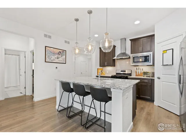 a open kitchen with stainless steel appliances granite countertop a stove a refrigerator a kitchen island a sink dishwasher a dining table and chairs with wooden floor