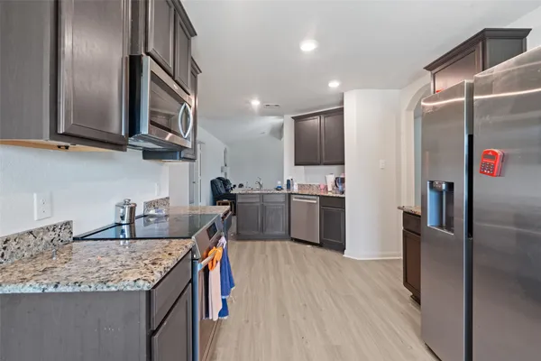 a kitchen with stainless steel appliances granite countertop a refrigerator a sink dishwasher a stove and a dining table with wooden floor