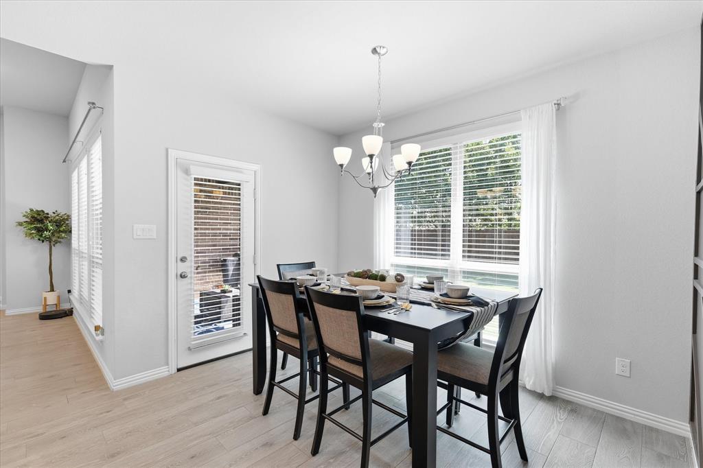 2908 Winding Ridge Court Oak Point, TX 75068 - Photo 11 of 38 Dining area featuring wood-finish flooring, a contemporary chandelier, large windows with blinds, a white-framed glass door, and crisp white walls