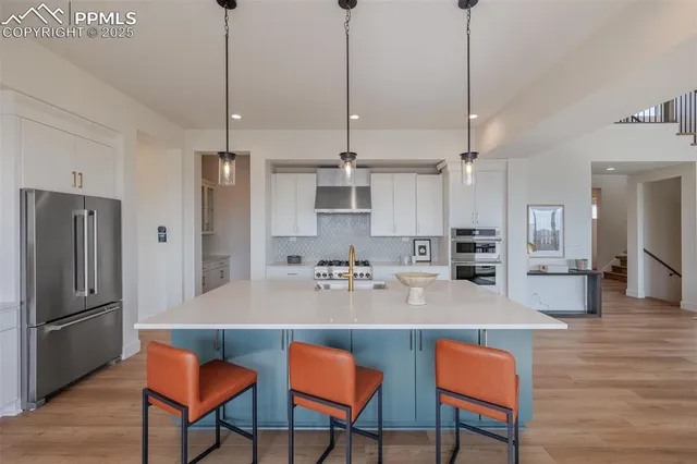 a kitchen with stainless steel appliances kitchen island granite countertop a refrigerator a stove a kitchen island and chairs with wooden floor